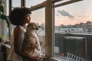 Woman cuddling a white dog while standing near a clear glass window