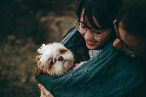 Woman carrying her dog through a dark green blanket wrapped around her body while her husband looks over her shoulder