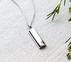 A silver with half cylinder-shaped pendant engraved with a dog's paw.