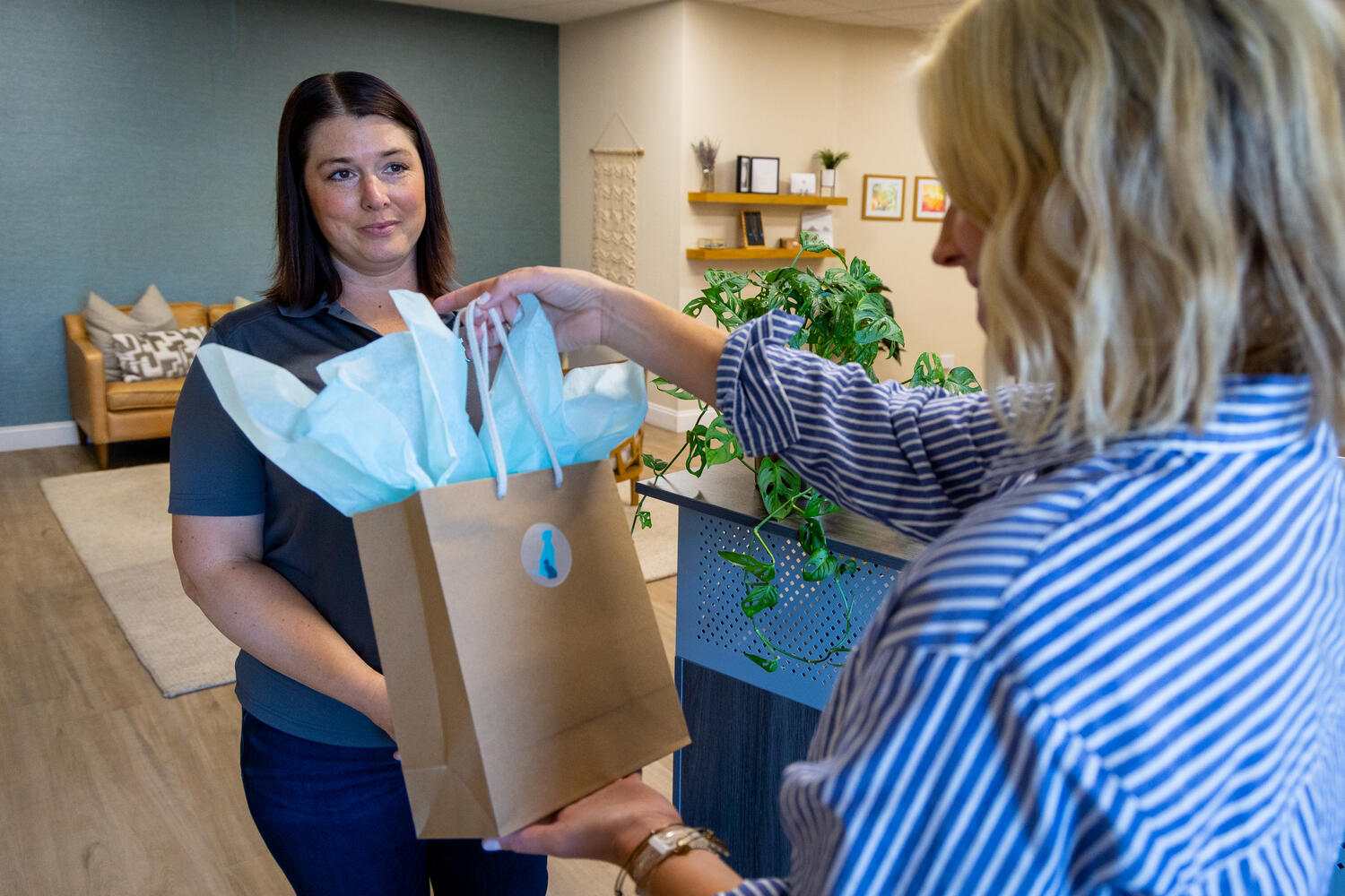 A woman receiving a gift bag with light blue tissue paper from another person.