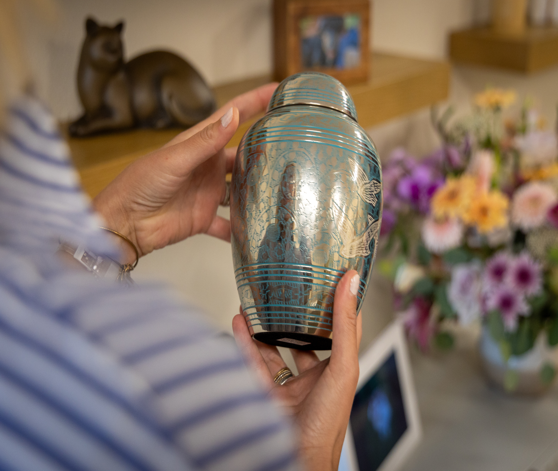 Hands holding an ornate blue and silver urn with bird designs