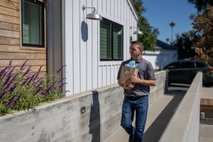 Man carrying a paper bag while walking outside a house
